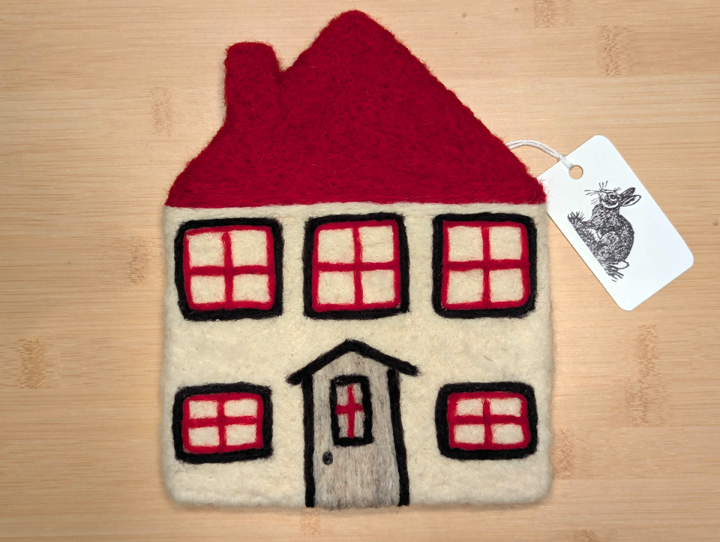 A felted white house with a red roof, black and red trim around the windows, and a grey door.