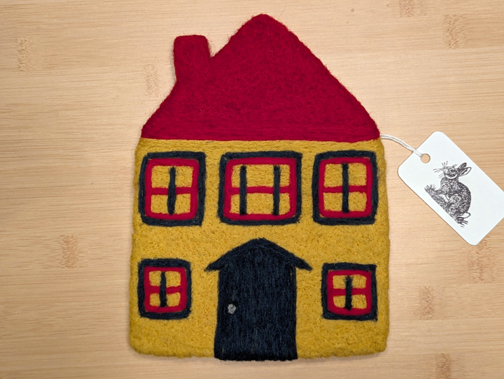 A felted yellow house with a red roof, green and red trim around the windows, and a green door.