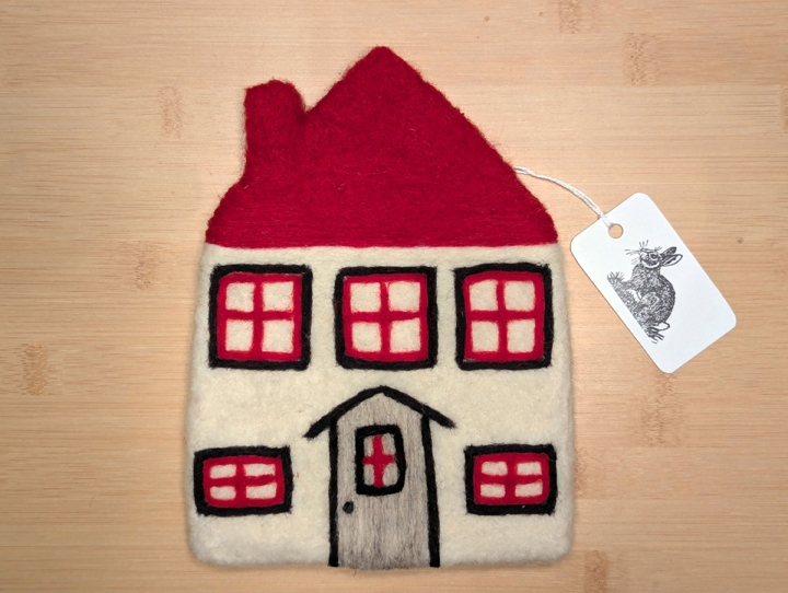 A felted white house with a red roof, black and red trim around the windows, and a grey door.