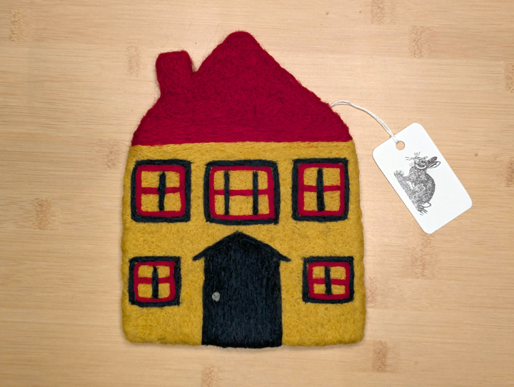 A felted yellow house with a red roof, green and red trim around the windows, and a green door.