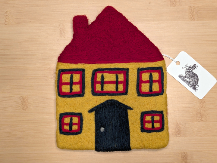 A felted yellow house with a red roof, green and red trim around the windows, and a green door.